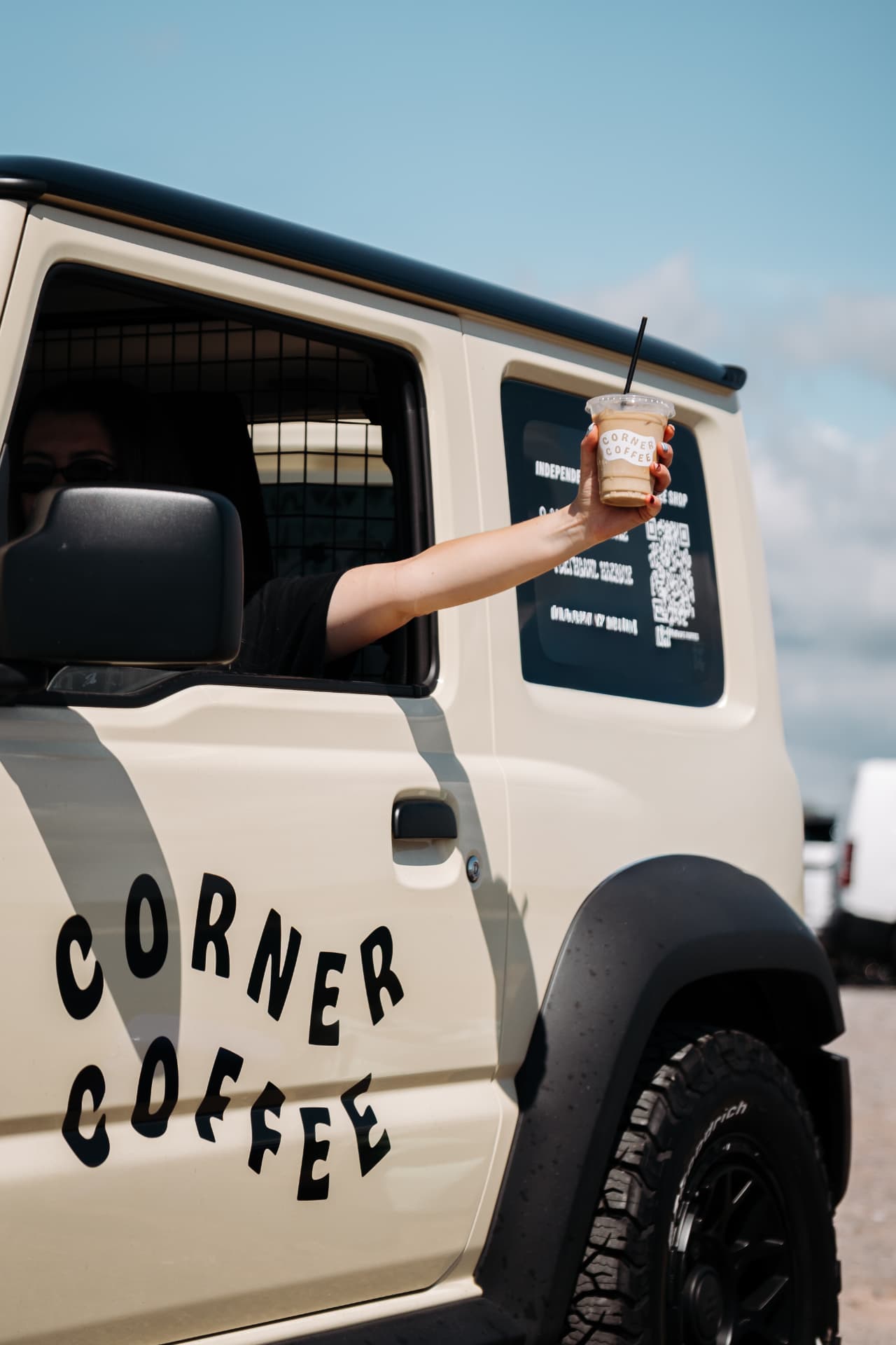 Iced coffee held out of the Corner Coffee Jimny window